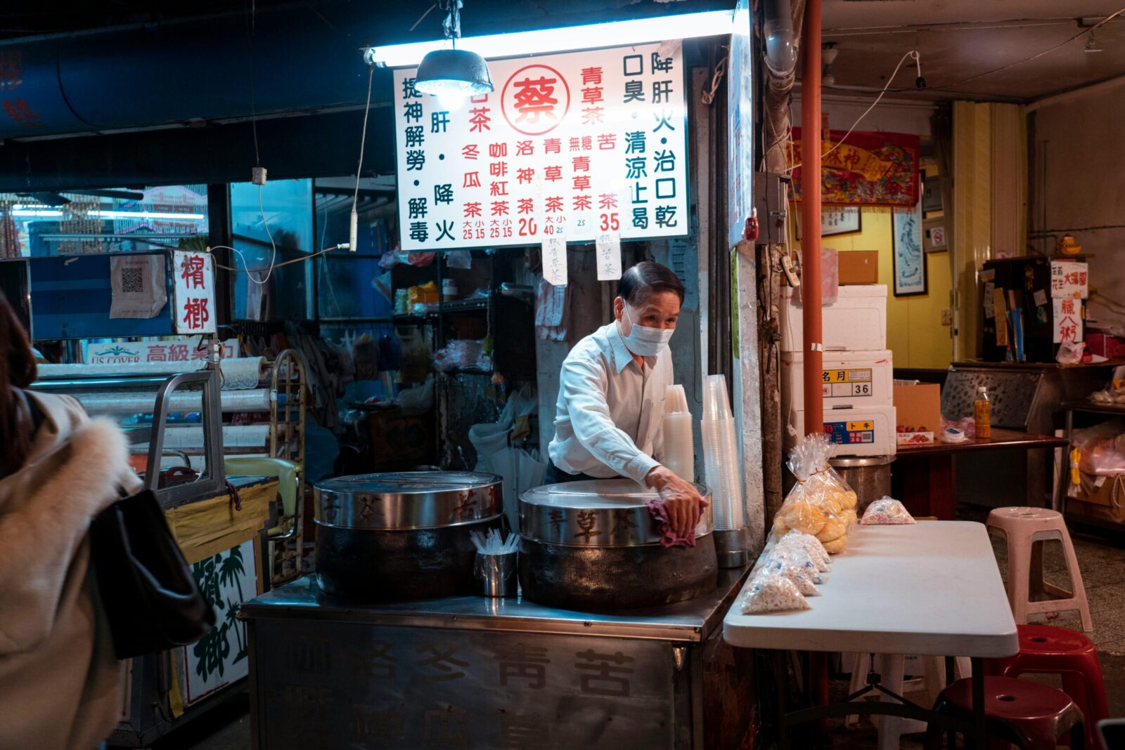 Street vendor in night market preparing snacks next to illuminated signs, capturing urban night ambiance.